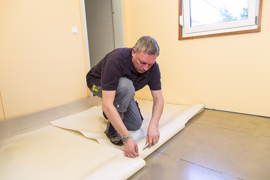Den akklimatisierten Bodenbelag einpassen. Den Bodenbelag halbseitig zurückschlagen und das Schutzpapier von Sigan 1 flach und gerade bis zum zurückgeschlagenen Bodenbelag abziehen.